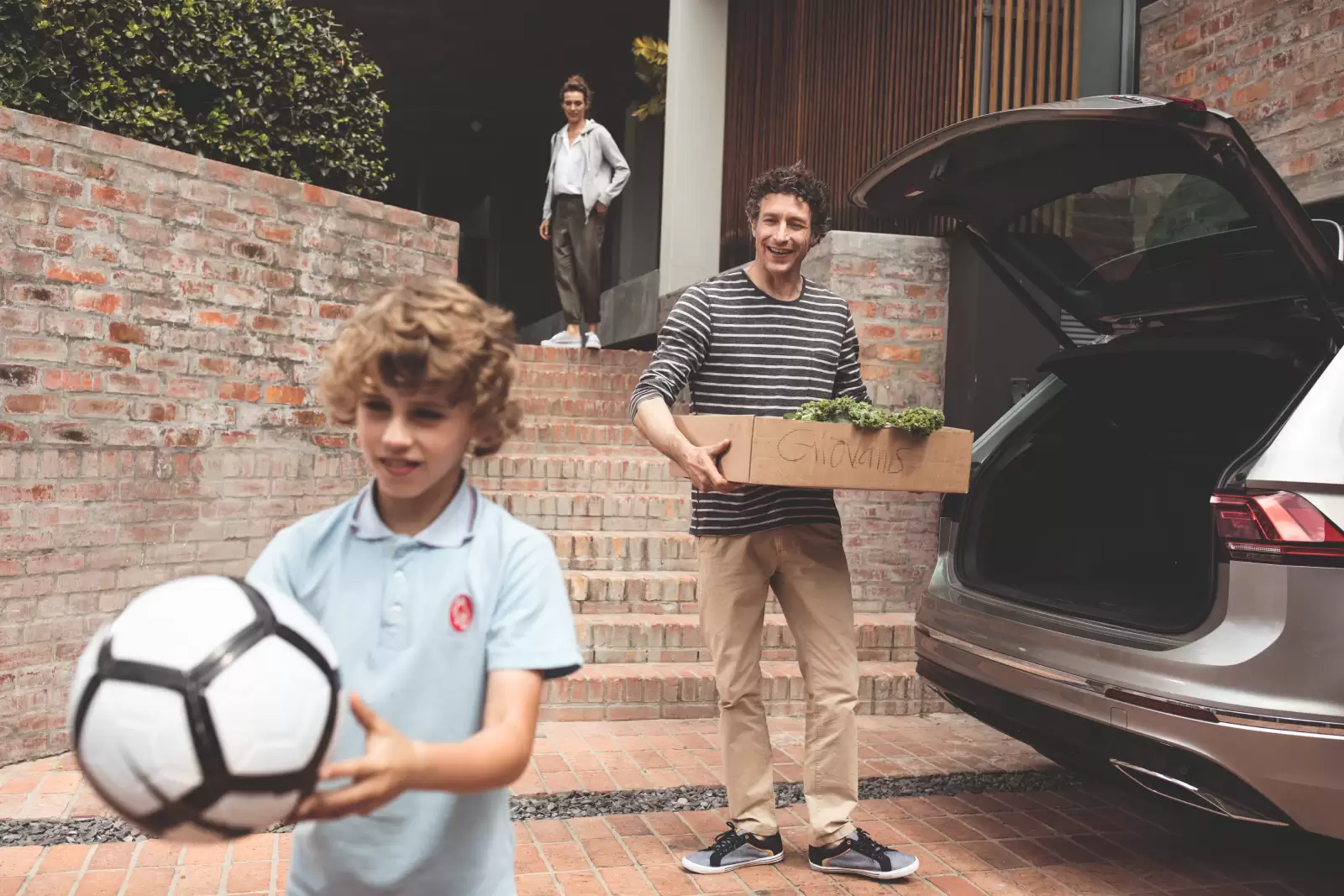 Seguro Garantia Estendida Volkswagen: filho, pai e mãe em frente à casa guardando coisas no porta-malas de um carro. 
